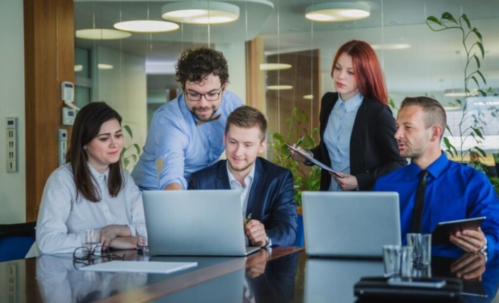 Diverse team of business professionals and project managers collaborating around laptops during a corporate meeting in a modern office environment.