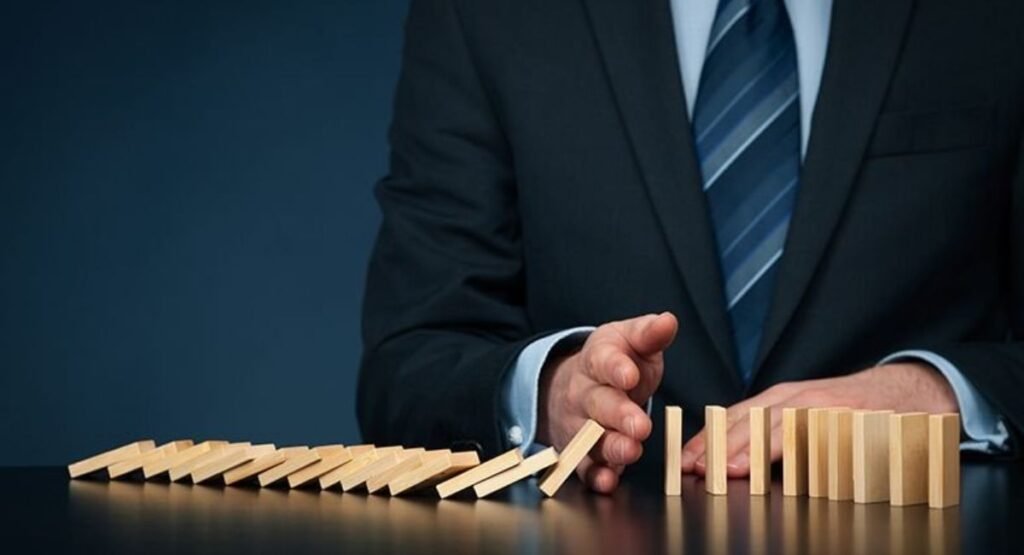 Businessman stopping falling wooden dominoes to represent risk management and crisis control.