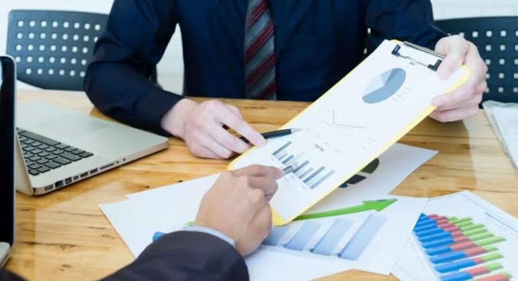 Two business professionals analyzing financial charts and data on a clipboard at a wooden desk.