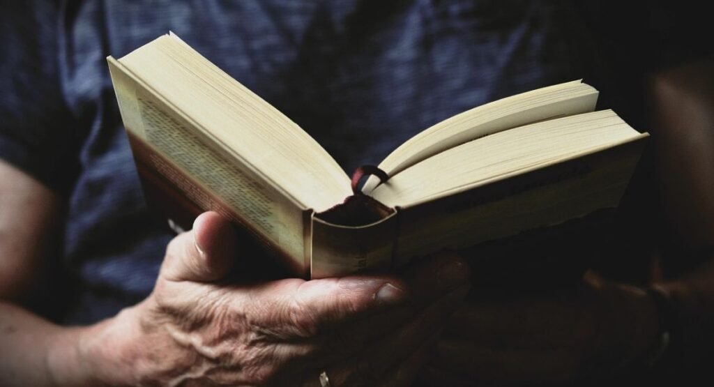 Close-up of a person holding an open hardcover book with a ribbon bookmark.