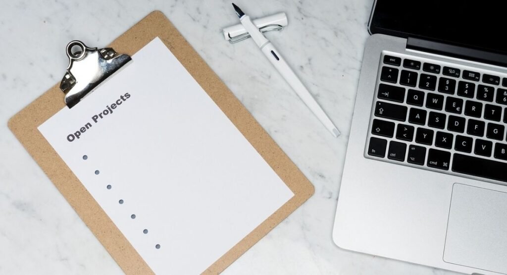 Top-down view of an Open Projects checklist on a clipboard next to a white fountain pen and a laptop on a marble desk.